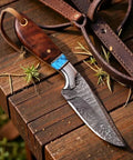 Damascus Cowboy Knife with Rosewood Handle and Leather Pancake Sheath, fixed blade on wooden table, used for outdoor survival.