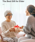 Elderly woman receiving a wrapped gift from a younger woman, both smiling in a cozy setting.