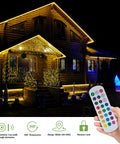House decorated with Smart Outdoor Rope Light 49.2ft RGB LED Strip illuminating edges, remote control in hand visible