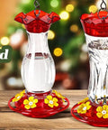 Three red and clear hummingbird feeders with floral designs displayed on a wooden surface, ideal for garden decoration.