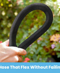 Close-up view of a black braided garden hose held in a hand in a garden setting.