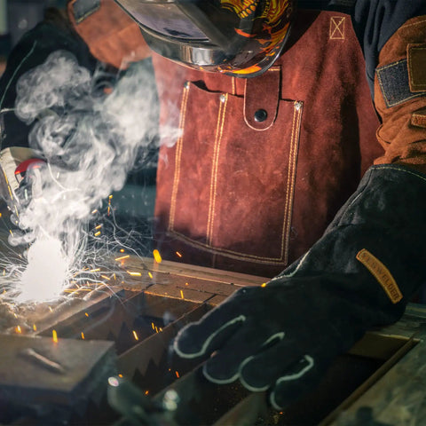 Person welding with sparks in protective gear wearing double layer leather welding sleeves with heat and flame resistance