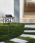 Solar Address Sign With LED Illuminated House Number For Outdoor Use Waterproof Address Plaque For Your Home Yard And Street 135 Degree Adjustable Solar Panel Auto Mode Light On At Night shown on a lawn.