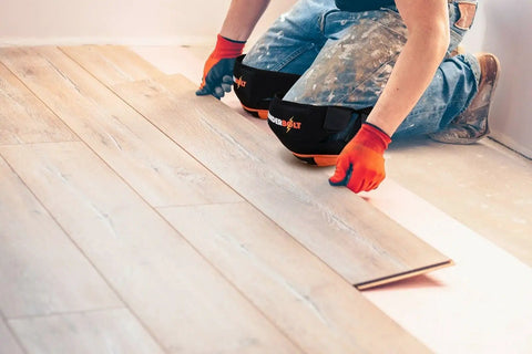 Person installing flooring wearing heavy duty knee pads for work and home use with double gel comfort extra thick foam adjustable non slip straps.