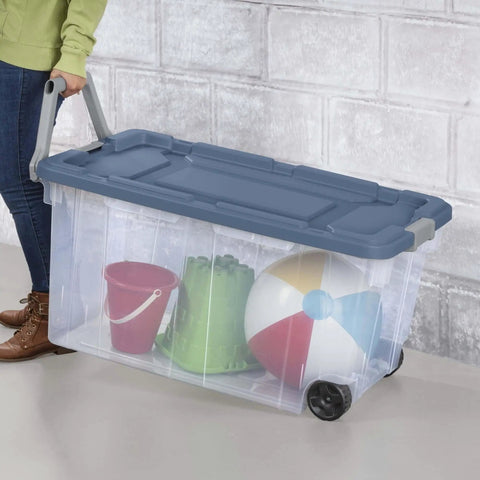 Person carrying a clear wheeled storage tote filled with toys, featuring a secure lid and easy grip handles.