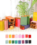 Medium Kraft Gift Bags With Handles, 16 Colorful Options, 10.6 x 8.3 x 4.3 Inches, assortment of 16-pack on display with plants