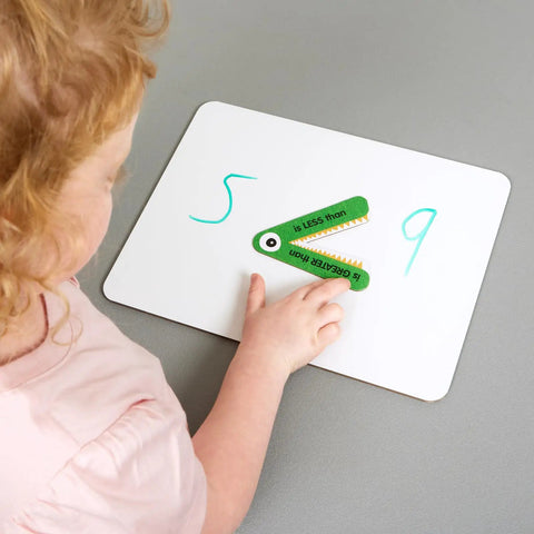 Child using Greater Than Or Less Than Gator Mouth Math Manipulatives Set Of 12 For Grades K 3 Ages 5 8 to compare numbers on a whiteboard