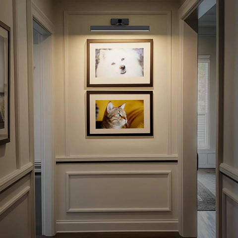 16 Inch Wall Mounted Picture Light With Slick Cct Dimming And Long Lasting Rechargeable Battery Paired With A Wireless Remote illuminating framed pet photos in a hallway.
