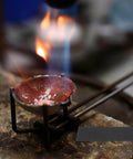 Molten metal in a crucible under flame with graphite block ingot plate for vacuum furnaces, electrolysis, and electroplating visible