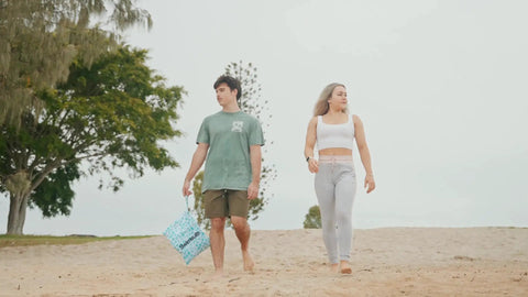 Two people walking on beach, person holding Two Pack Ultra Waterproof Wet Dry Bags With Dual Zippered Pockets for swim gear.