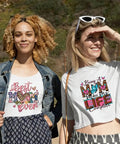 Two women wearing t-shirts with mom-themed designs including hearts and text outdoors.