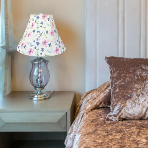 Floral lamp shade on clear glass table lamp next to bed with velvet brown bedding in cozy bedroom setting