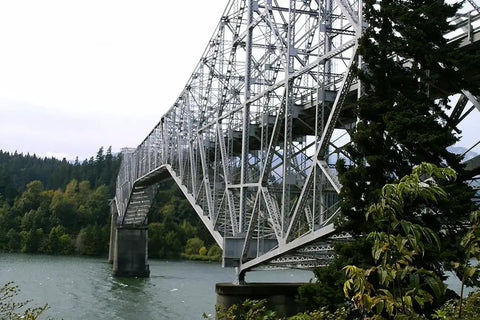 Steel truss bridge over a river with surrounding trees and hills