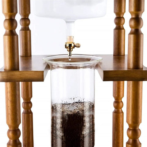 Top Shelf Stainless Steel Cold Brew Dripper With Heavy Duty Premium Borosilicate Glass dripping coffee with wooden support.