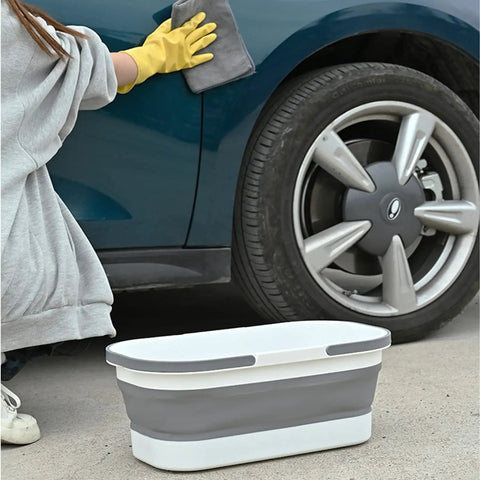 Collapsible Rolling Bucket With Four Wheels 12L Mop Bucket For Home Cleaning Camping And RV Lightweight Portable Multi Purpose Rectangular Handy Basket For Mop And Laundry Gray next to a car