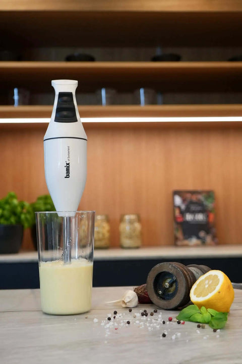 Top Shelf Swiss Made Classic Immersion Blender With 150W Motor And Two Speed Settings Whip Up Soups Smoothies Purees Like A Pro With Multipurpose Blade Beater And Whisk In White blending a creamy mixture in a glass
