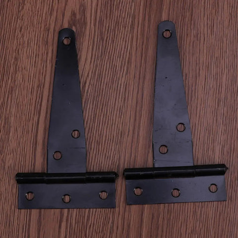 Two black iron 4 inch T-shape hinges with six screw holes for outdoor gates and indoor doors shown on a wooden surface.
