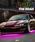Car with pink Aura Pro Underglow LED Lights Kit on a road, showcasing neon underbody lighting and scenic background at dusk.