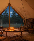 Cozy tent interior with view of full moon through open flaps, featuring kettle on fire and seating area with blankets and pillows.