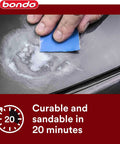 Person applying nitrocellulose glazing putty on car body panel using a blue sanding pad.