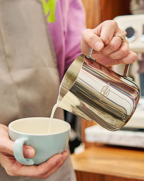 32 Oz Milk Frother Pitcher With Clear Scale, 304 Stainless Steel Steaming Jug And Latte Art Pen in use pouring milk into coffee.