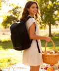 Woman wearing Insulated Leakproof Cooler Backpack With Waterproof Oxford Fabric Large Capacity Holds 30 Cans Lightweight Travel Camping Beach Ice Chest For Men And Women Black Includes Beer Opener And Reusable Trash Bag, holding picnic basket outdoors.