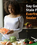 Woman in kitchen holding vacuum-sealed bag with sliced carrots, surrounded by vegetables and kitchen tools