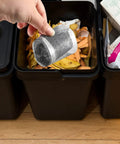 Hand holding a silver Hair Catcher for Shower-Self-Adhesive Drain Strainer Filter Roll above a compost bin filled with organic waste.