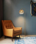 Gradient Gold Floor Lamp With Glass Globe LED Standing Light In Modern Mid Century Style beside a leather armchair in living room.