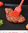 Red silicone oil brush applying marinade on steak in barbecue tools image.