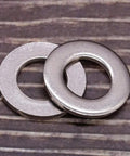Close-up of two 1/4-inch stainless steel flat washers with bright finish on wood surface.