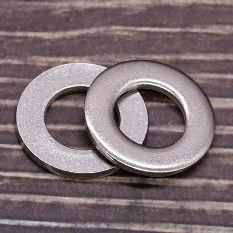 Close-up of two 1/4-inch stainless steel flat washers with bright finish on wood surface.