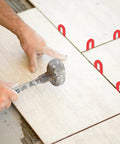 Front view of red plastic horseshoe tile shims between ceramic tiles; used with a mallet.