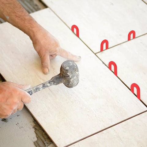 Front view of red plastic horseshoe tile shims between ceramic tiles; used with a mallet.