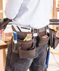 Worker wearing Heavy Duty Leather Tool Apron With Seven Pockets, Hammer Holder And Rivet Reinforced Edges For Pro Grade Toughness.