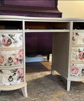 Floral vintage desk with curved drawers, featuring pink rose decals and a cream finish, set in a cozy room with vintage decor.