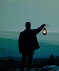 Person holding 12 Inch Hurricane Lantern With Durable Red Finish For Camping And Emergencies against a mountain backdrop