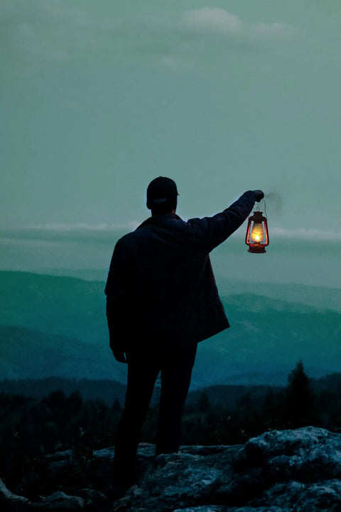 Person holding 12 Inch Hurricane Lantern With Durable Red Finish For Camping And Emergencies against a mountain backdrop