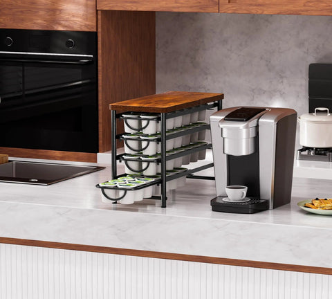 Universal Coffee Pod Holder With Two Multifunctional Storage Drawers For Tea Bags And K Cup Pods Nespresso Dolce Gusto CBTL Verismo Holds Up To 60 Pods In A Retro Brushed Bronze Finish displayed on a kitchen counter next to a coffee machine.