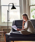 Industrial Floor Lamp For Living Rooms And Bedrooms, Rustic Farmhouse Standing Reading Lamp With Adjustable Metal Heads, Indoor Task Lighting For Home Office Deco In Black Finish next to a woman on a couch.
