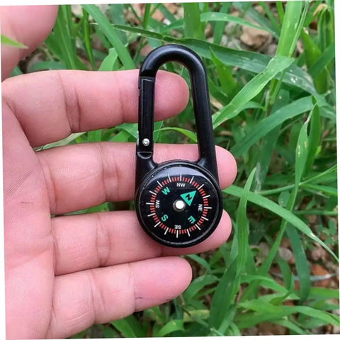 Hand holding a black carabiner with compass. Two Pack Outdoor Hiking Compass With Carabiner Keychain Go-To Pocket Navigation Tool For Camping