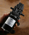 Person holding a 12V Diaphragm Water Pump 1.5 GPM At 100 PSI Self Priming DC Fresh Water Pump For RV Camper Boat Marine Lawn