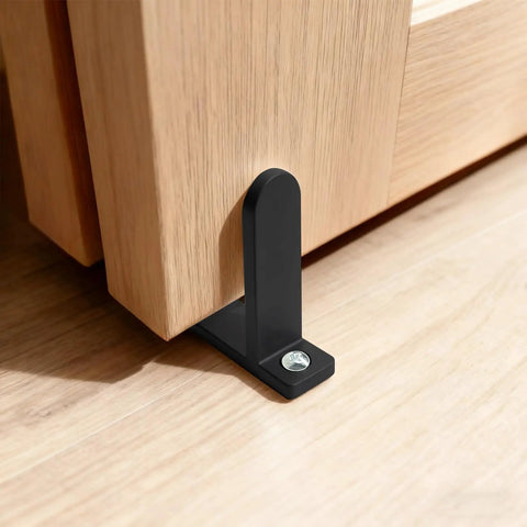 Close-up of Four Pack Universal Black Closet Door Floor Guide installed with screws for 1 3/8 inch thick sliding doors on a wooden floor.