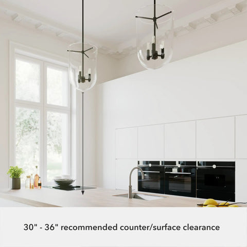 Two Sacha Pendant Light In Natural Iron Finish With Clear Glass Shade over modern kitchen island, showcasing suggested clearance.