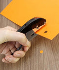 Hand using Beefy Built To Last Handheld Hole Punch 8mm Five Sixteenth Inch for cards and tags on orange paper
