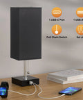 Set Of 2 Bedside Lamps With Dual USB Ports, black fabric shade, wood base, pull-chain switch, phone charging on wood table.