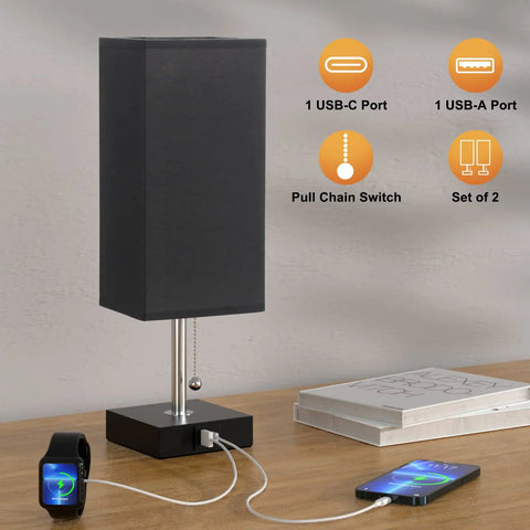 Set Of 2 Bedside Lamps With Dual USB Ports, black fabric shade, wood base, pull-chain switch, phone charging on wood table.