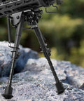 Carbon Fiber Bipod 6 To 9 Inches With M-Rail Adapter attached to rifle on rocks, showing lightweight and strong design
