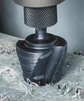 Heavy Duty Step Drill Bit With Quick Release Spiral Flutes And Hex Shank cuts steel wood showcased on metal surface with shavings.