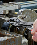 Close-up of hand using 8 Inch Pliers With Front And Side Gripping, Front Jaw Grips Stripped Screws, Side Jaw On Metal Machinery